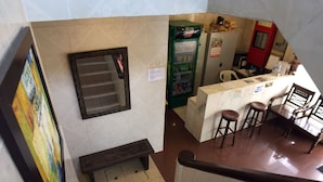 Un hall d’hôtel avec un escalier, un distributeur automatique, un comptoir avec des tabourets et un banc.