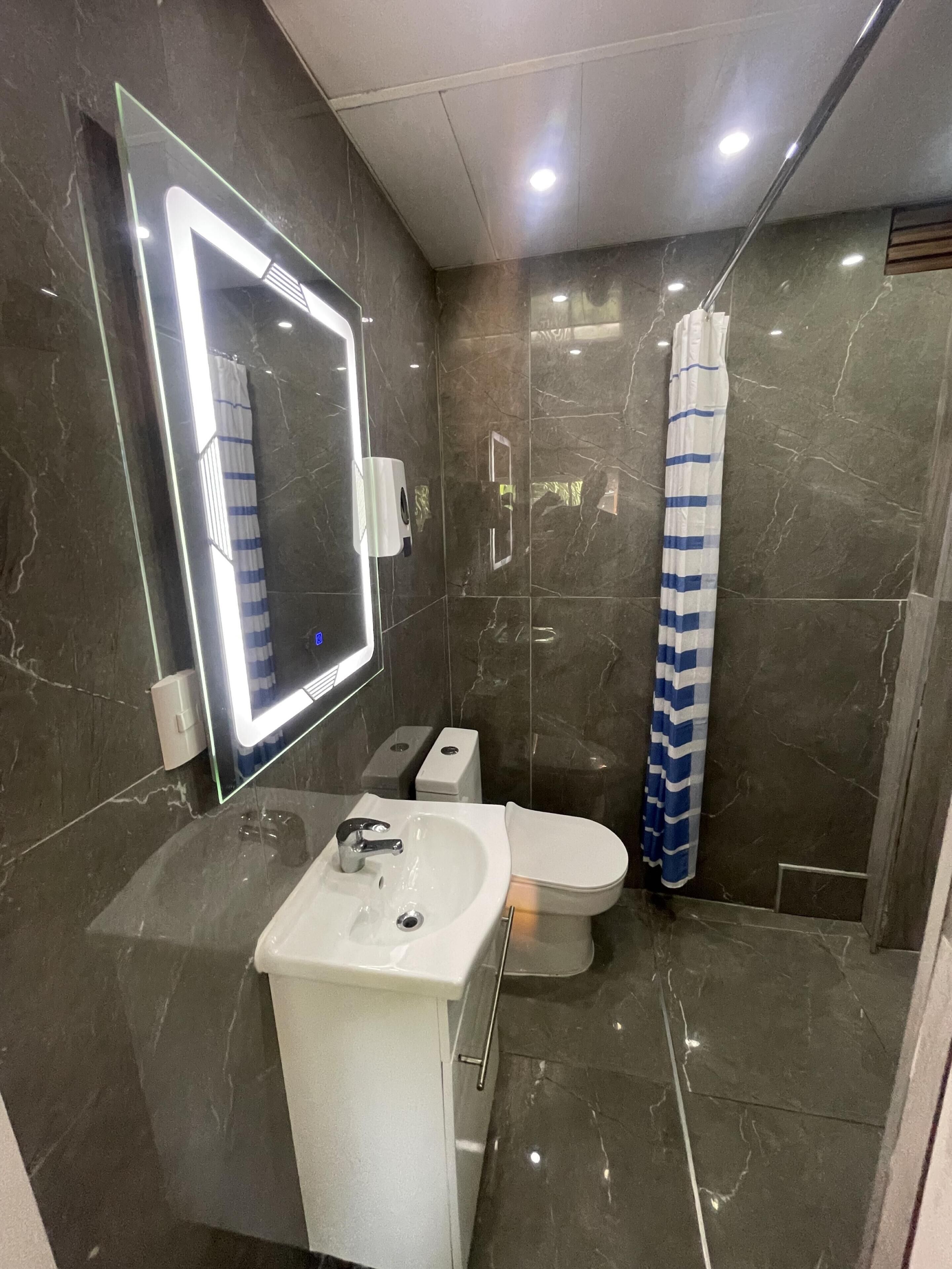 A modern bathroom with a white sink, a mirror with lights, a toilet, and a shower curtain.