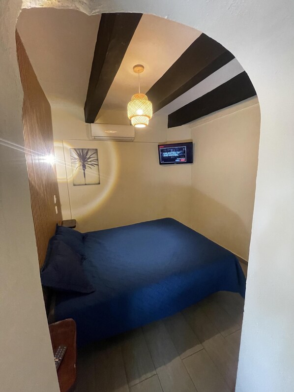 A small, cozy room with a single bed, a TV mounted on the wall, and a ceiling light fixture. - Island Life Hostel (Santo Domingo)