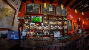 Een bar met een verscheidenheid aan drankflessen, een krijtbordmenu en een televisiescherm waarop een sportwedstrijd wordt vertoond.