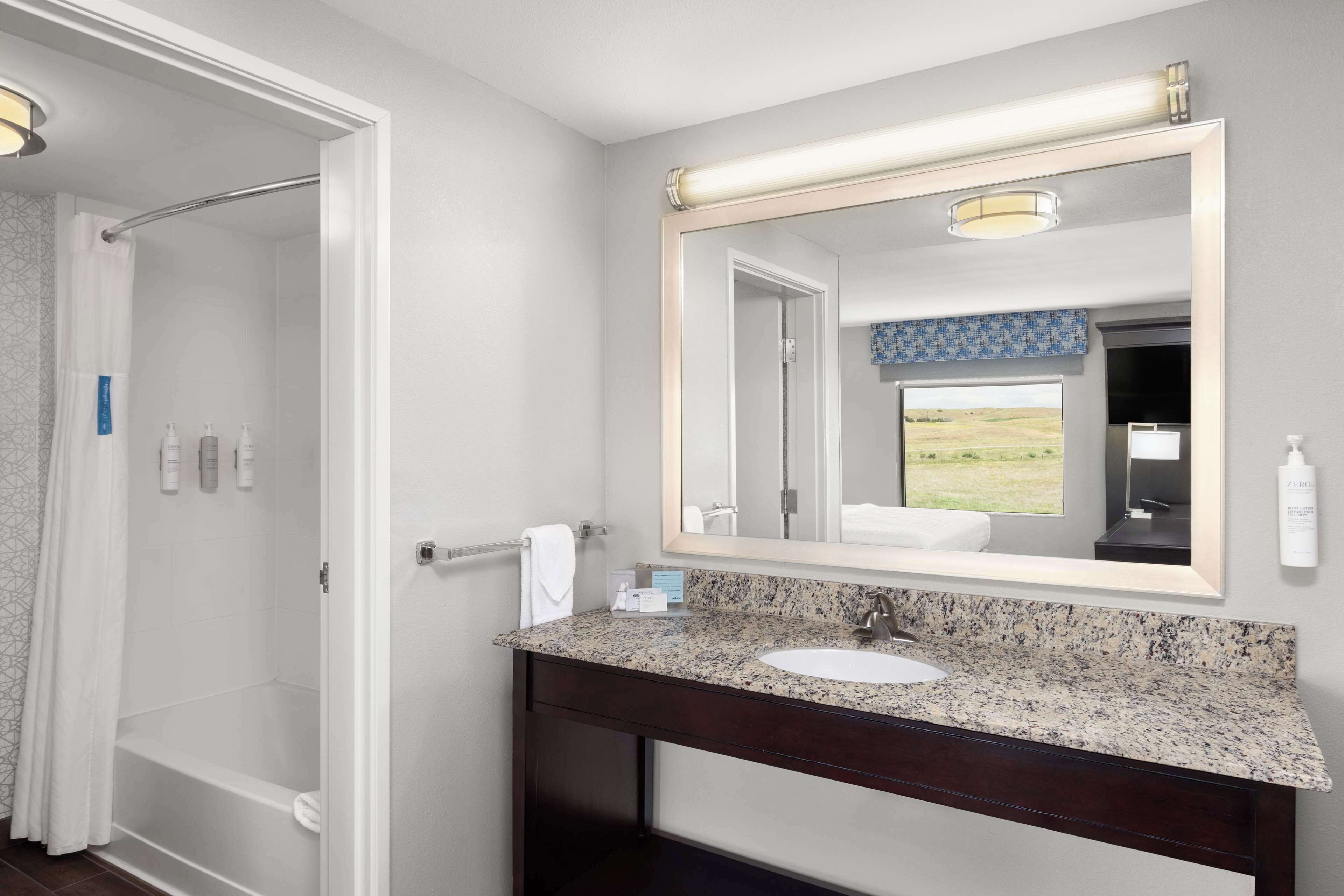 Une salle de bain avec un lavabo doté d’un plan de travail en granit, un grand miroir et un espace douche.