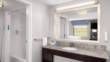 Une salle de bain avec un lavabo doté d’un plan de travail en granit, un grand miroir et un espace douche.