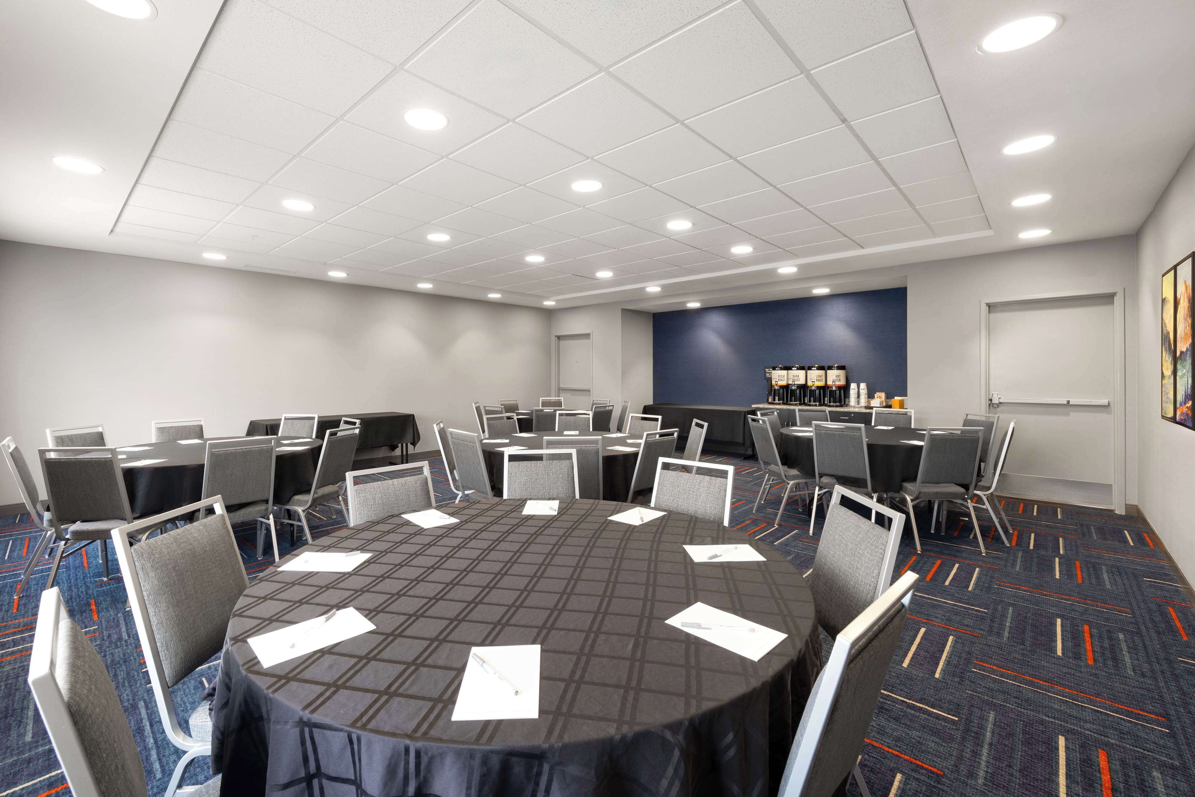 A conference room with a round table, multiple chairs, a carpeted floor, and a whiteboard on the wall.