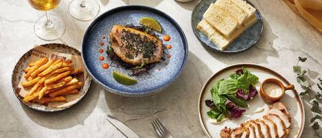 A table set with a variety of dishes including fish, fries, and a salad, accompanied by drinks and books.