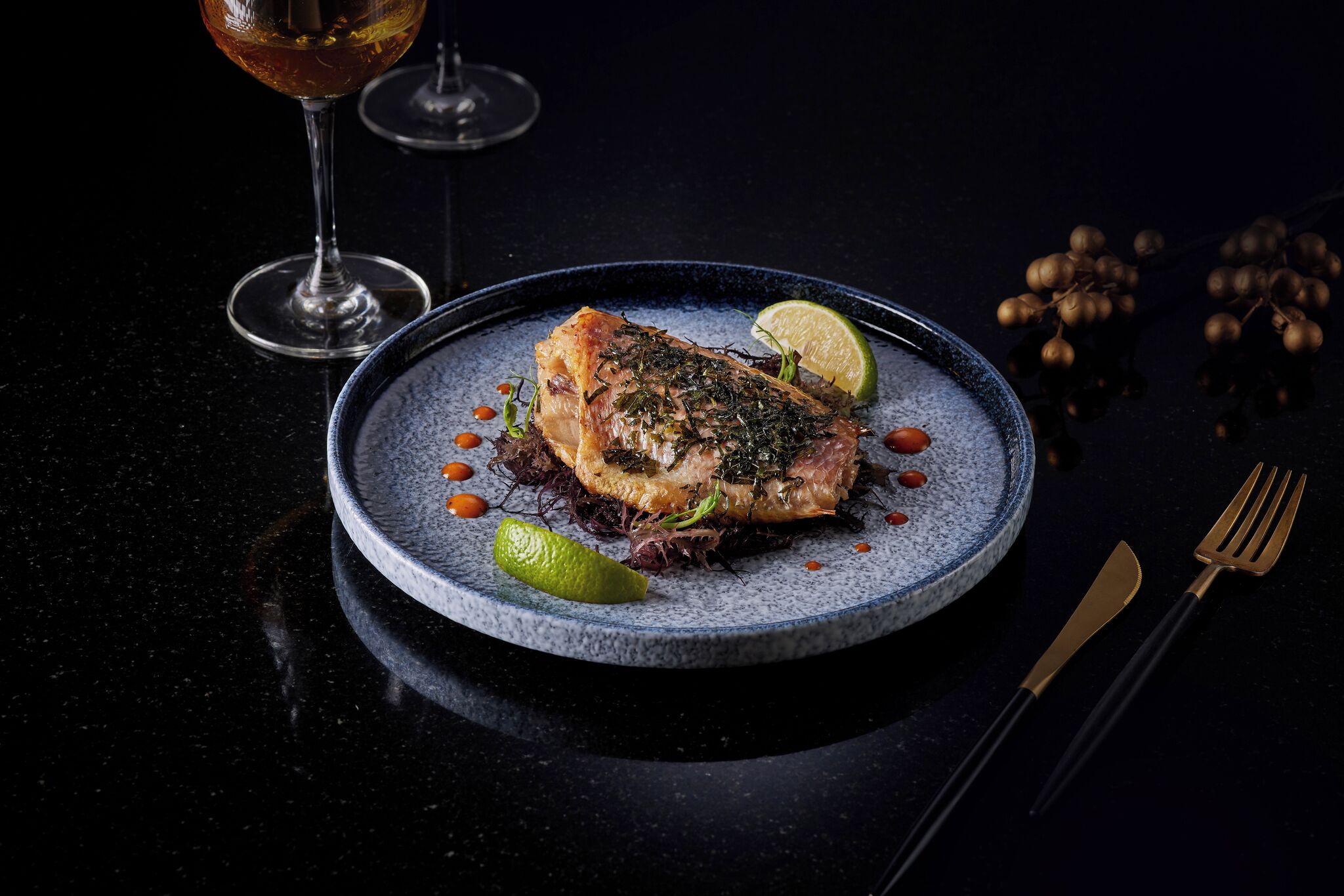 A plate of food with a slice of meat, a lime wedge, and some garnish on a dark plate.