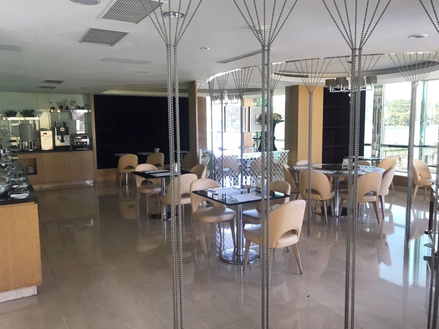 Uma área de refeições moderna com mesas e cadeiras, um bar e amplas janelas que proporcionam muita luz natural.