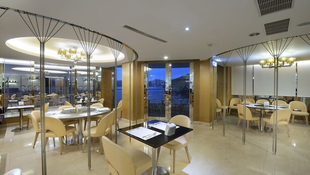 A modern dining area with round tables, beige chairs, and a view of the cityscape through large windows. - The Crystal Inn Sun Moon Lake (Yuchi)