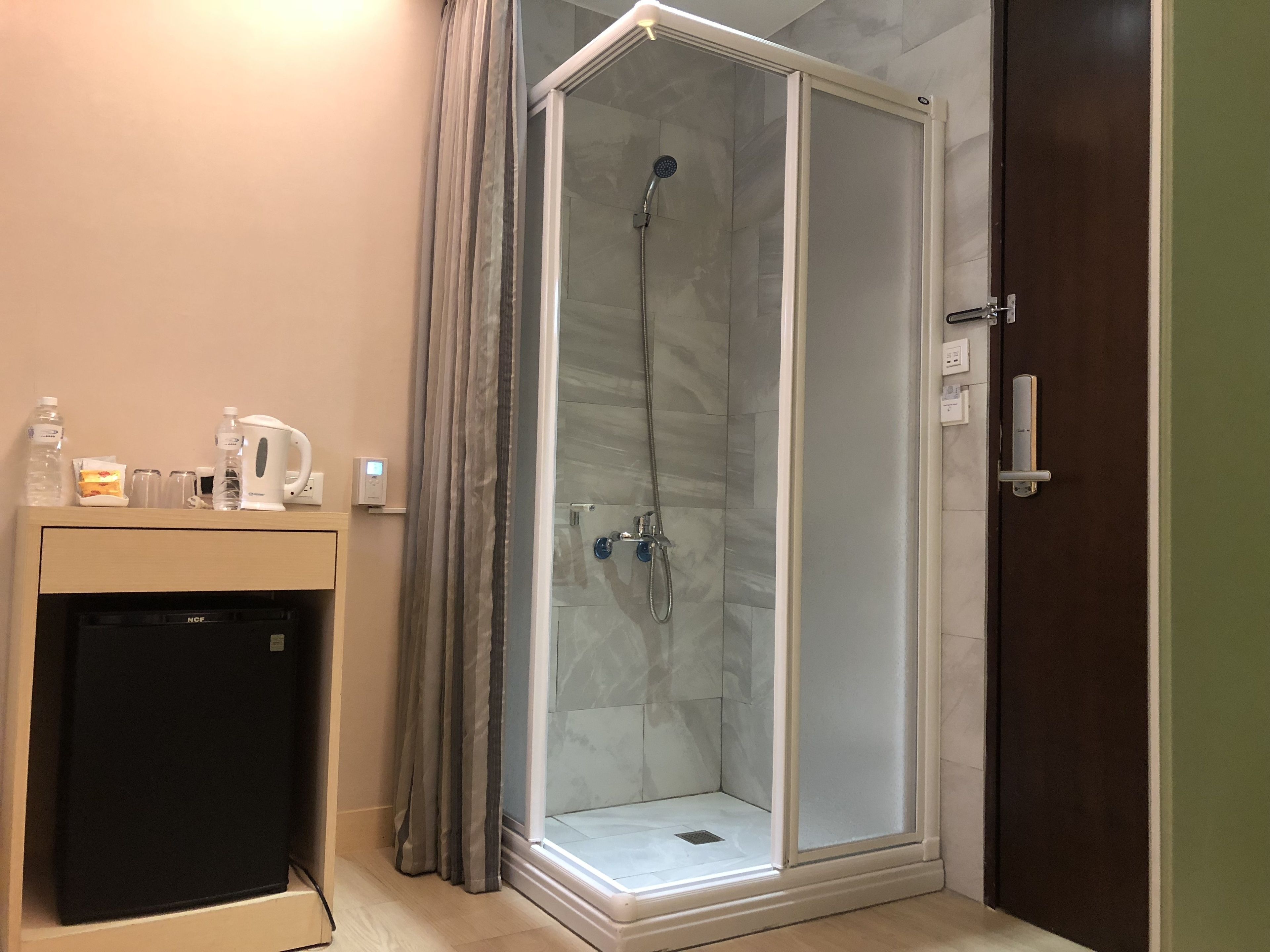 A shower room with a glass door, a small sink with a kettle, and a refrigerator.