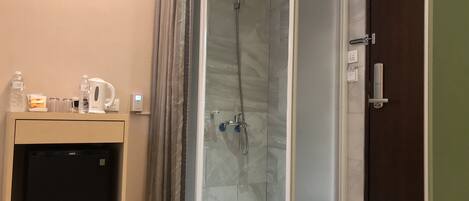 A shower room with a glass door, a small sink with a kettle, and a refrigerator.