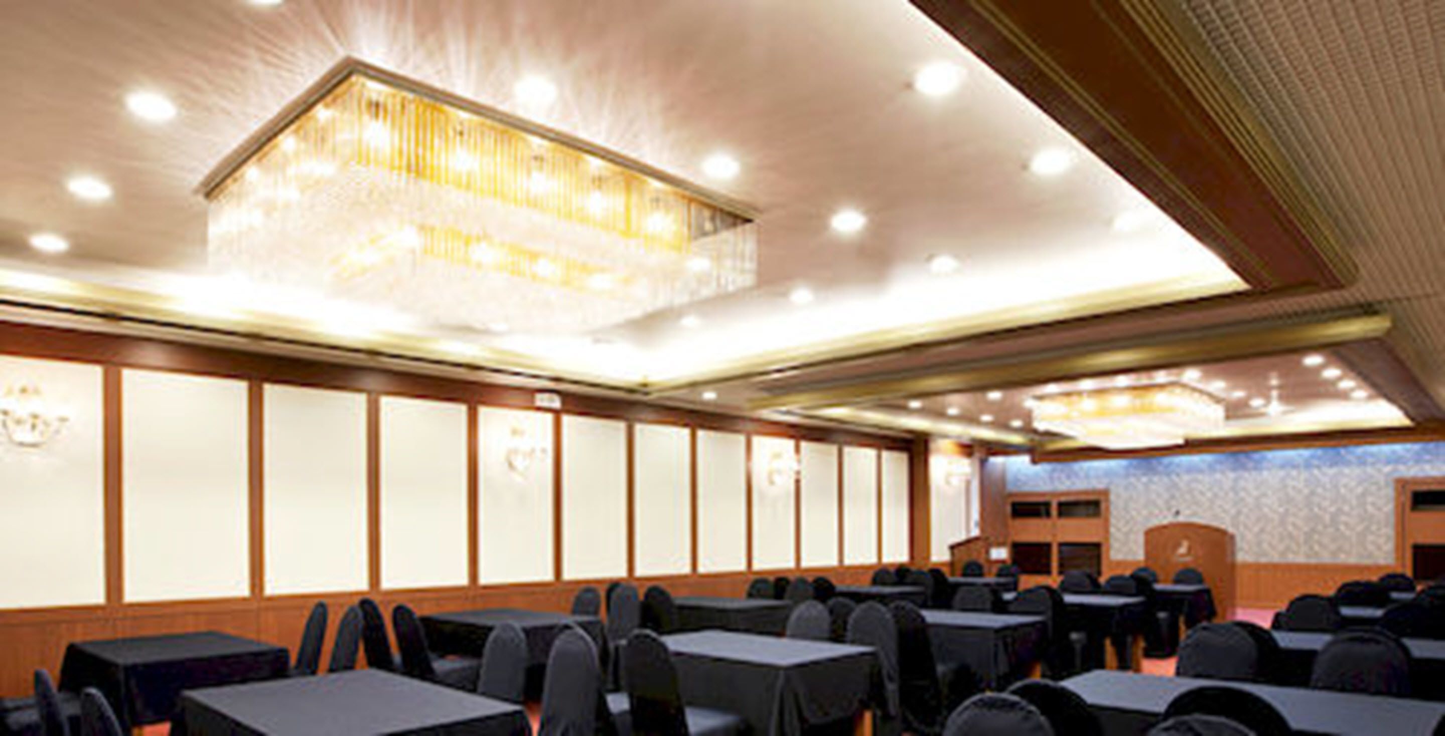 A conference room with rows of tables and chairs, a podium, and a large chandelier.