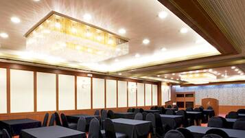 A conference room with rows of tables and chairs, a podium, and a large chandelier.
