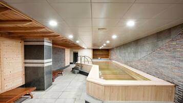 Un área de spa con un banco de madera, una pared de piedra y una bañera de hidromasaje.