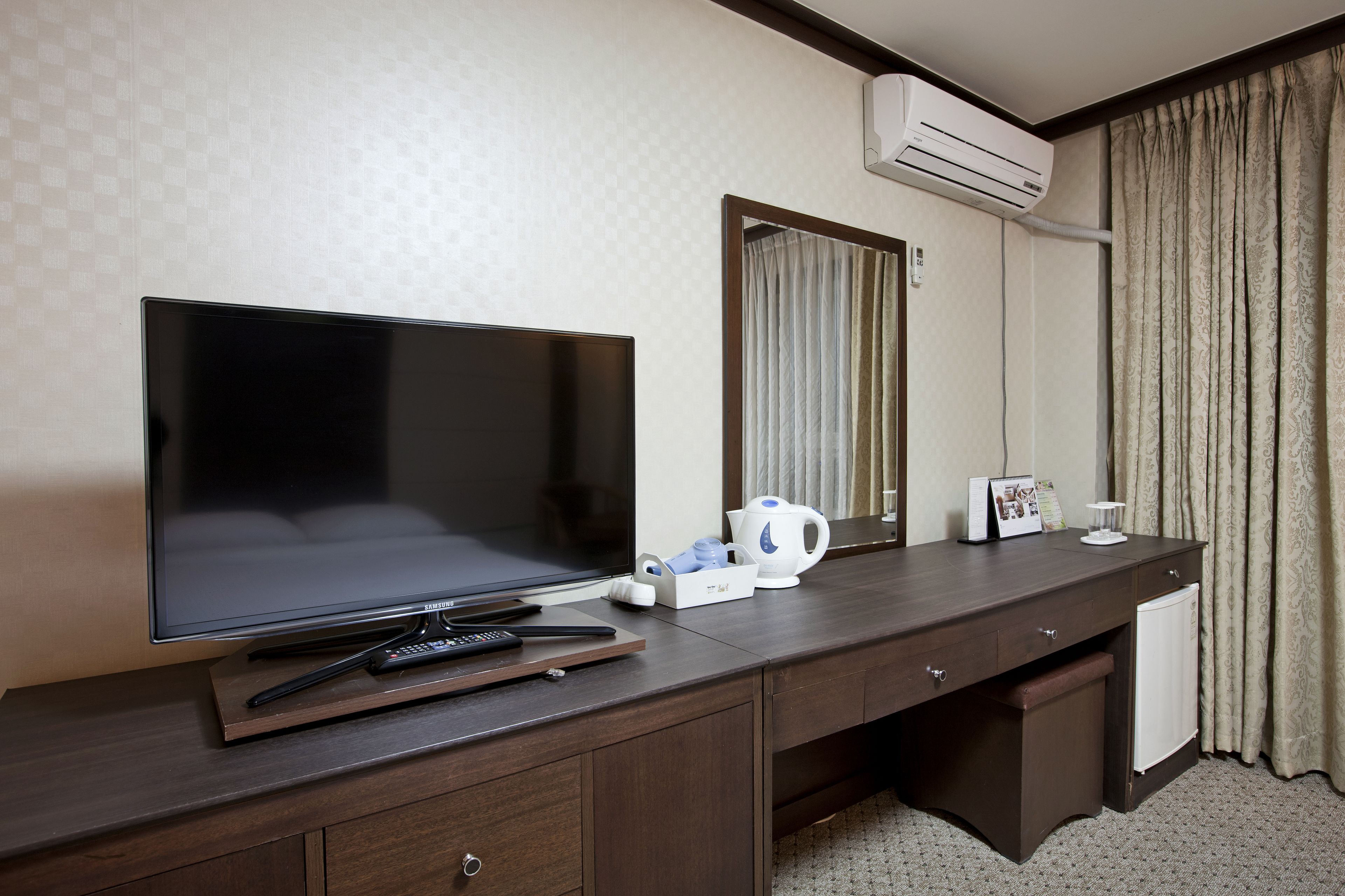 Een hotelkamer met een groot flatscreen televisietoestel, een koffiezetapparaat, een afstandsbediening en een klein kastje.