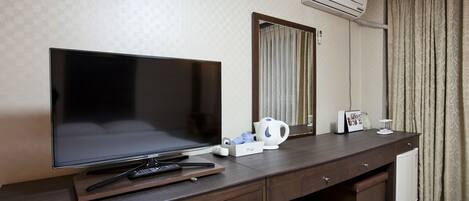 Habitación de hotel con televisor de pantalla plana grande, cafetera, control remoto y mueble auxiliar.