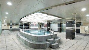 Een modern binnenzwembad met een centraal gelegen zwembad, treden die in het zwembad leiden en een plafond met inbouwverlichting.