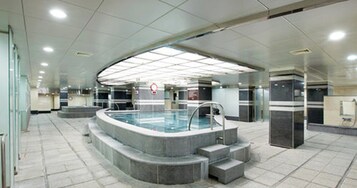 Un área interior de piscina moderna con una piscina central, escalones que bajan a la piscina e iluminación empotrada en el techo.