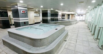 Uma piscina coberta grande com várias pistas de natação, rodeada por um chão ladrilhado e paredes de vidro.