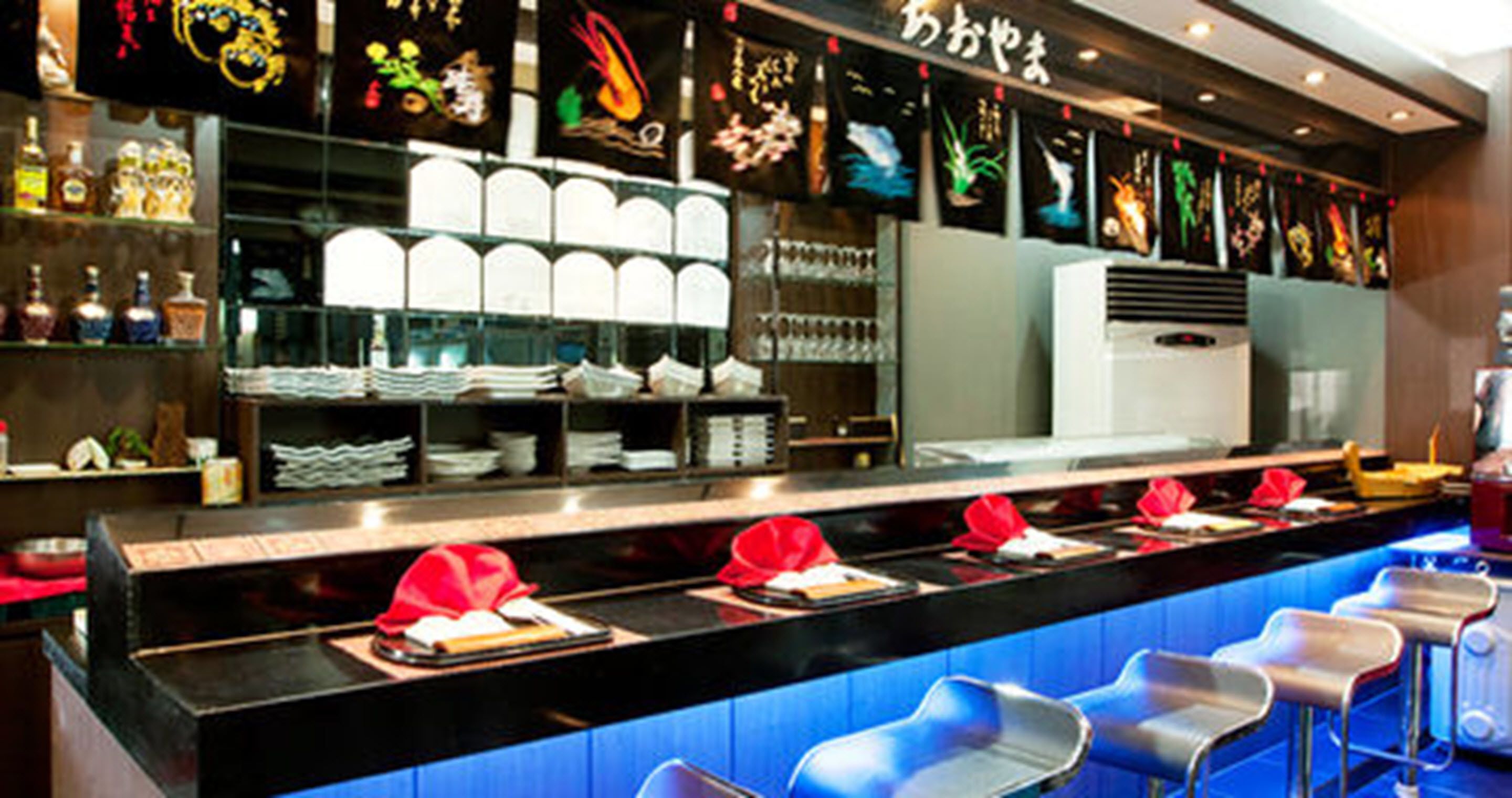 Una barra azul en el mostrador de un restaurante, con platos blancos apilados en estantes y servilletas rojas sobre el mostrador.