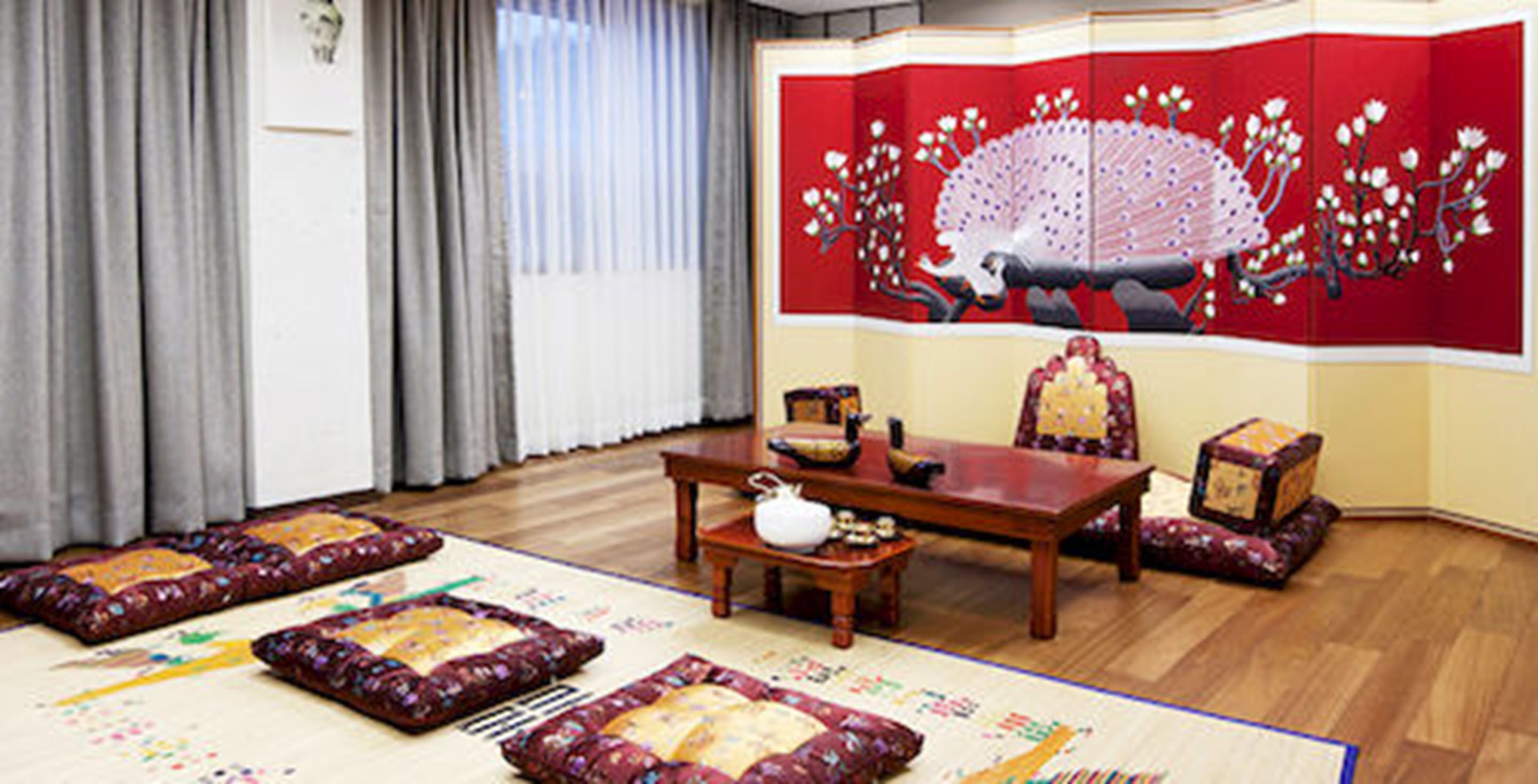 Una tradizionale stanza giapponese con pavimento in tatami, un tavolino in legno e un paravento scorrevole rosso decorato con un motivo di pavone.