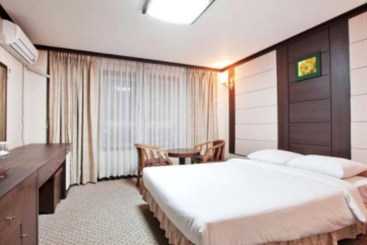 A hotel room with a bed, a desk, a chair, and a window with curtains.