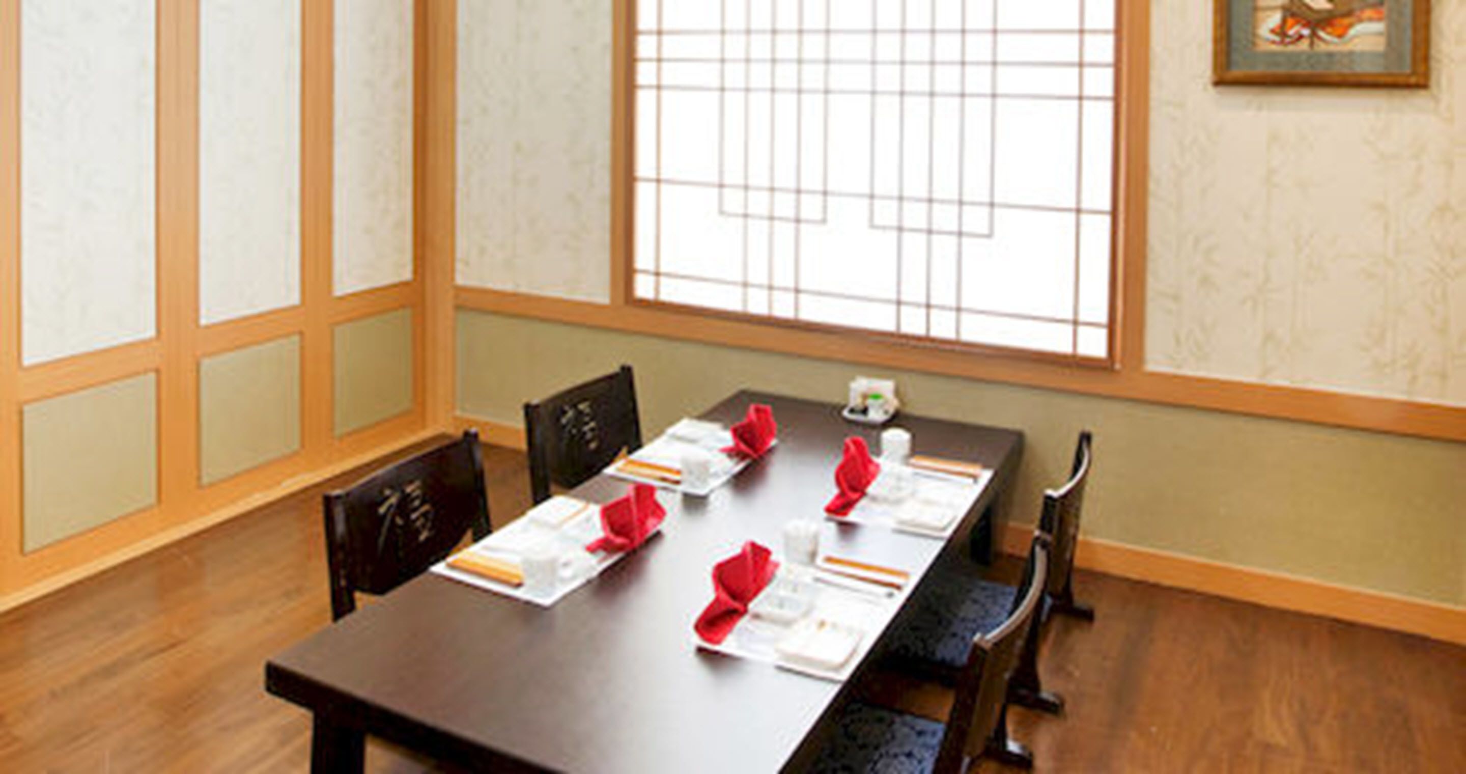 A dining area with a long table set for four, wooden chairs, and a window with grid-style blinds.