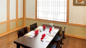 A dining area with a long table set for four, wooden chairs, and a window with grid-style blinds.