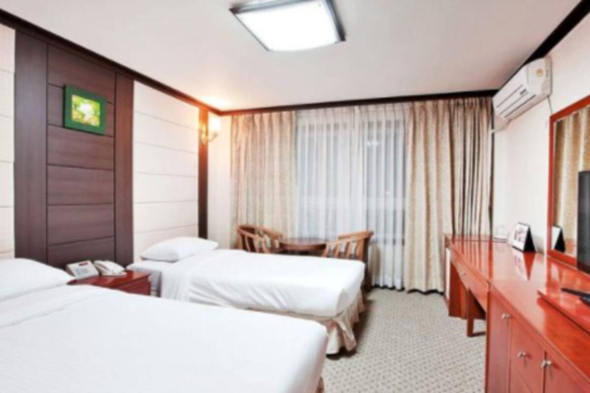 A hotel room with two beds, a desk, a chair, a TV, and a window with curtains.