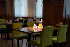 A restaurant with green upholstered chairs, wooden tables, and pendant lighting. - Holiday Inn Aktau by IHG (Aktau)