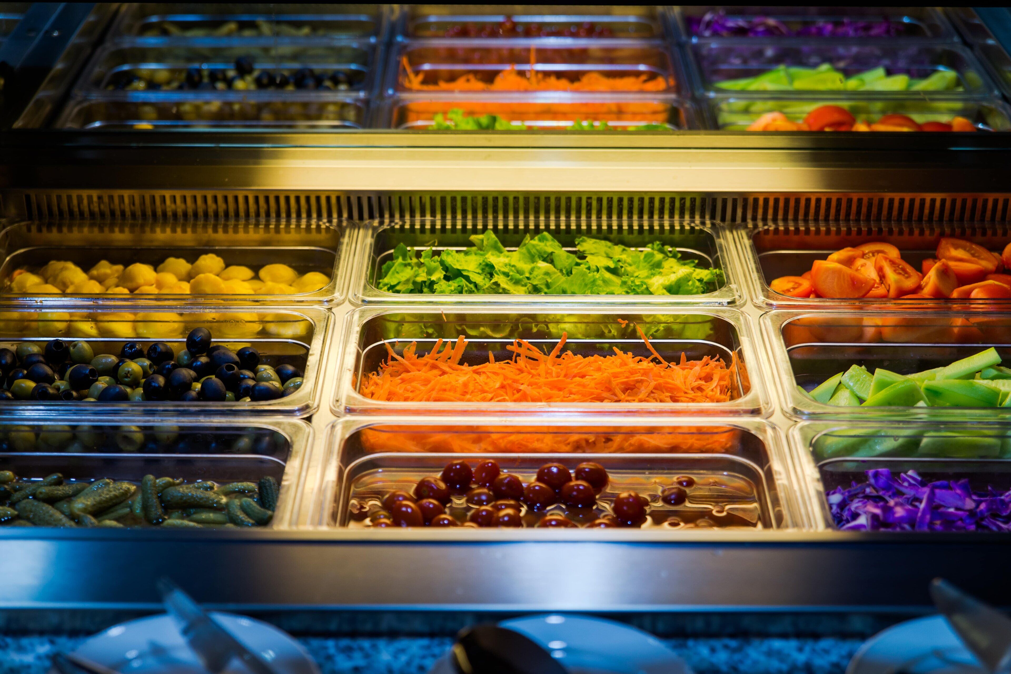 Una barra de ensaladas con diversos vegetales y frutas.