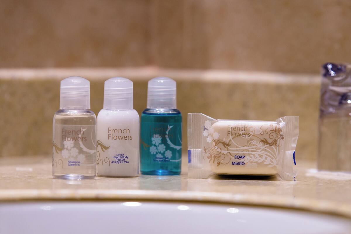A bathroom counter with three bottles of French Flowers shampoo and one bar of soap.