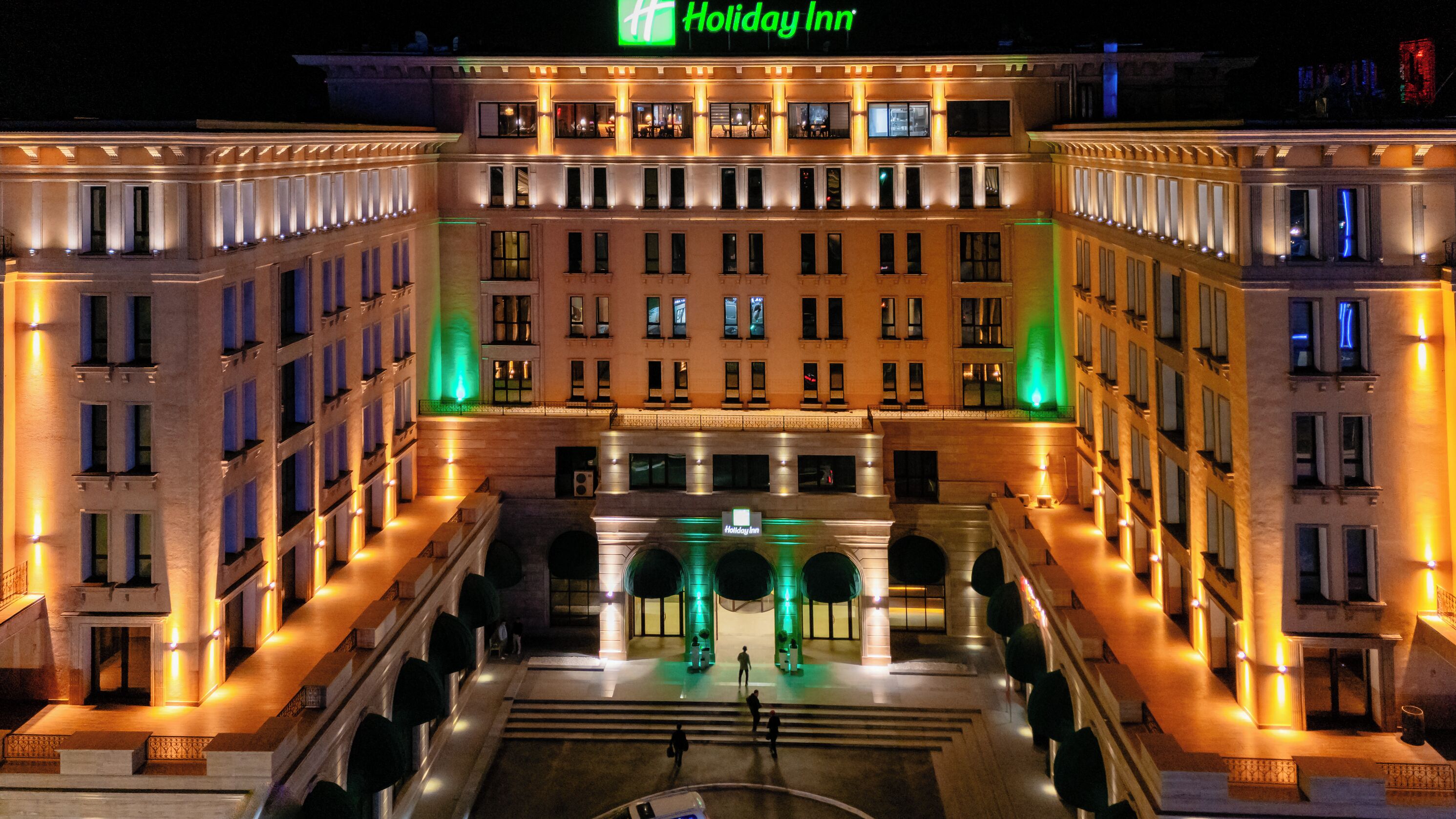 Ein Holiday Inn Hotel mit einer symmetrischen Fassade, mehreren Etagen und einem zentralen Innenhof mit einem Brunnen.