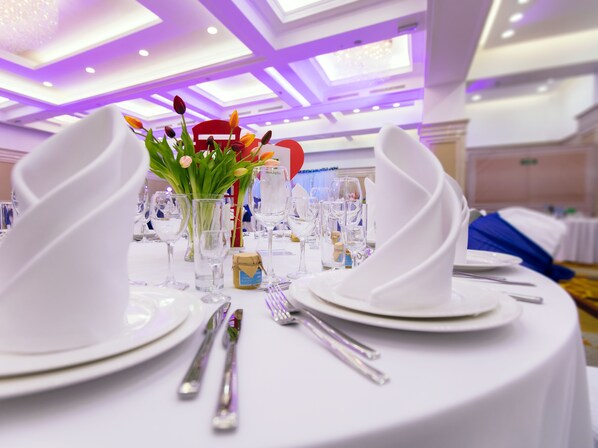 A round table set for a formal event with white tablecloths, clear glassware, and a centerpiece of flowers. - Holiday Inn Aktau by IHG (Aktau)