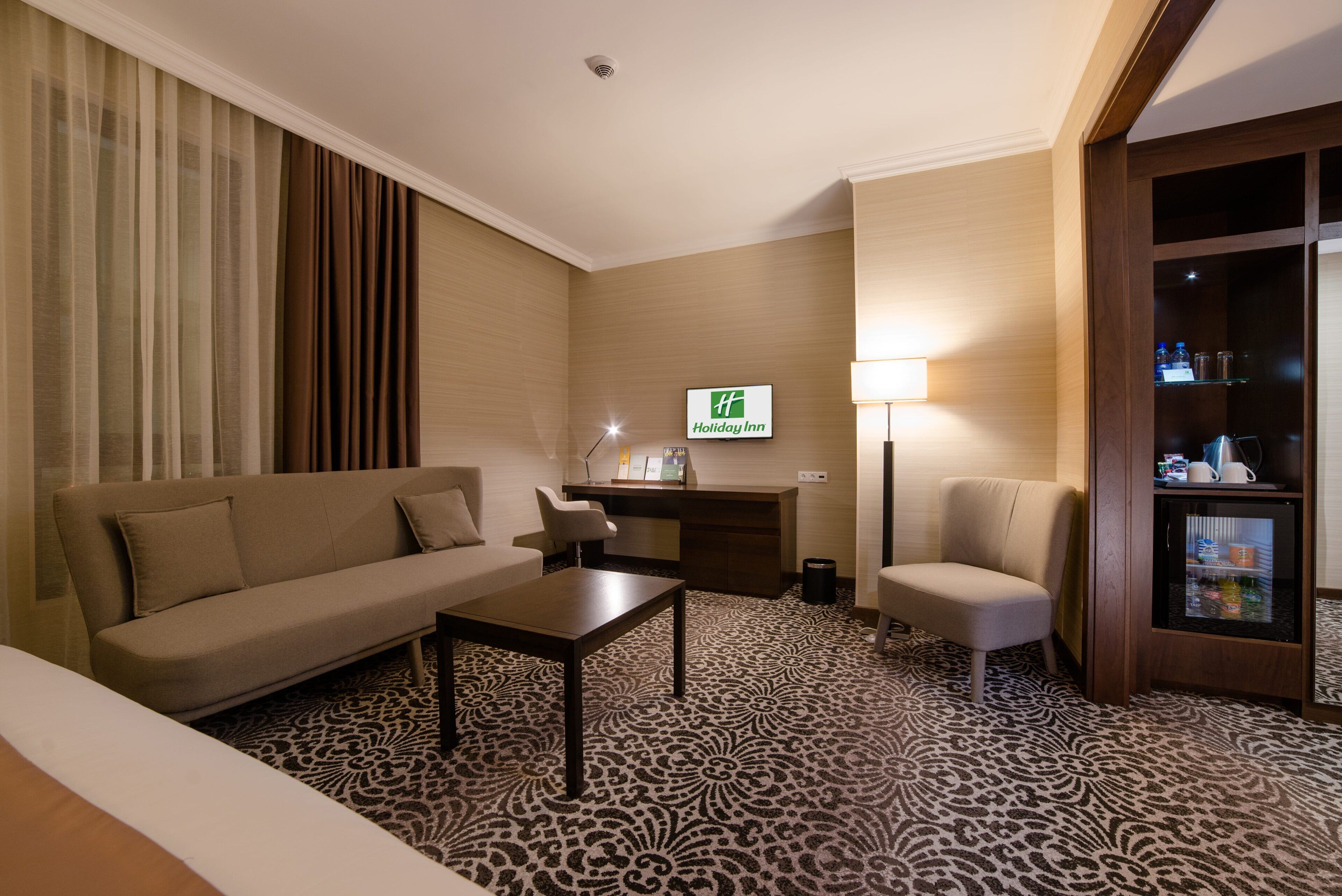 Habitación de hotel con sofá, sillón, mesa de centro, escritorio y minibar.