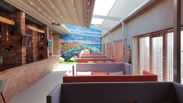 Un espacio de estar al aire libre con techo, paredes de ladrillo, un mural de una escena costera y vistas de la ciudad.