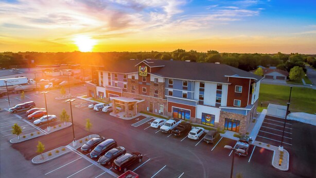 A hotel with a parking lot, a building with a 'My Place' sign, and a sunset in the background.