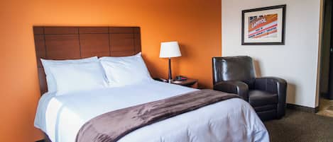 A hotel room with a large bed, a chair, a lamp, and a framed picture on the wall.