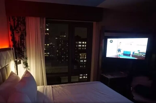A hotel room with a bed, a television, and a view of the city at night.