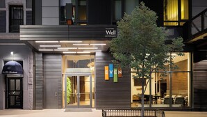 A modern hotel entrance with a tree in the foreground, a sign reading 'Well,' and a '327' sign above the door. - EVEN Hotel New York - Times Square South by IHG (New York)