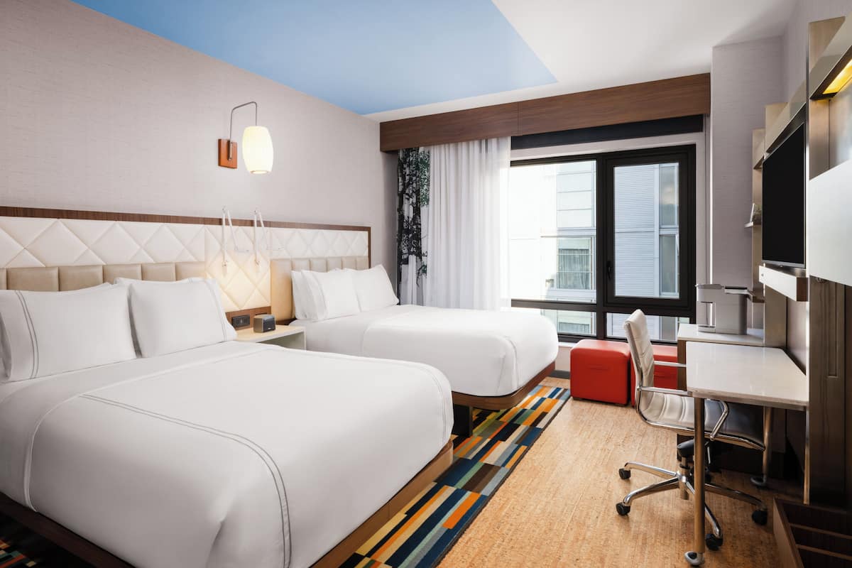 A hotel room with two beds, a desk, a TV, and a window with curtains.