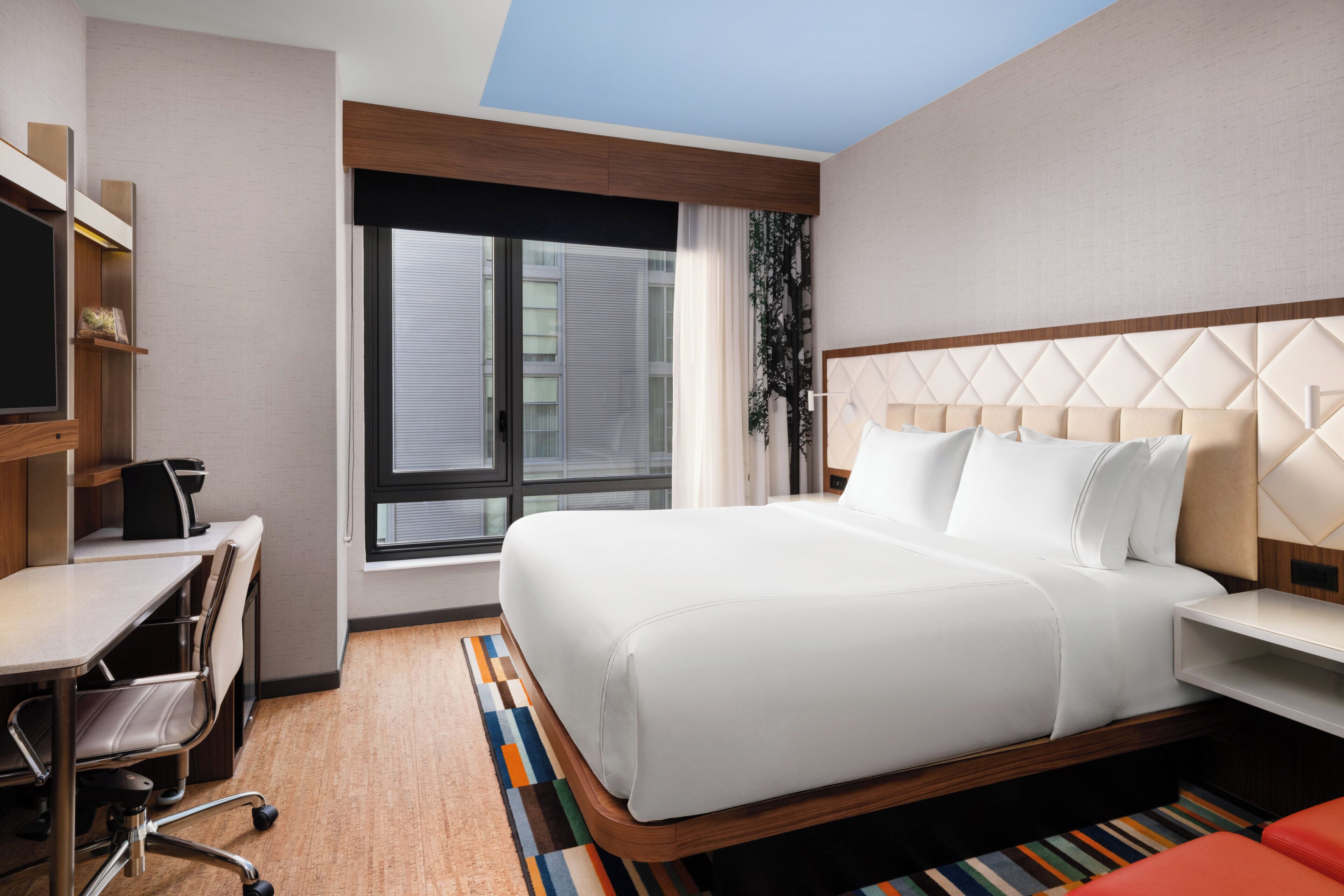 A hotel room with a bed, desk, chair, and a large window.