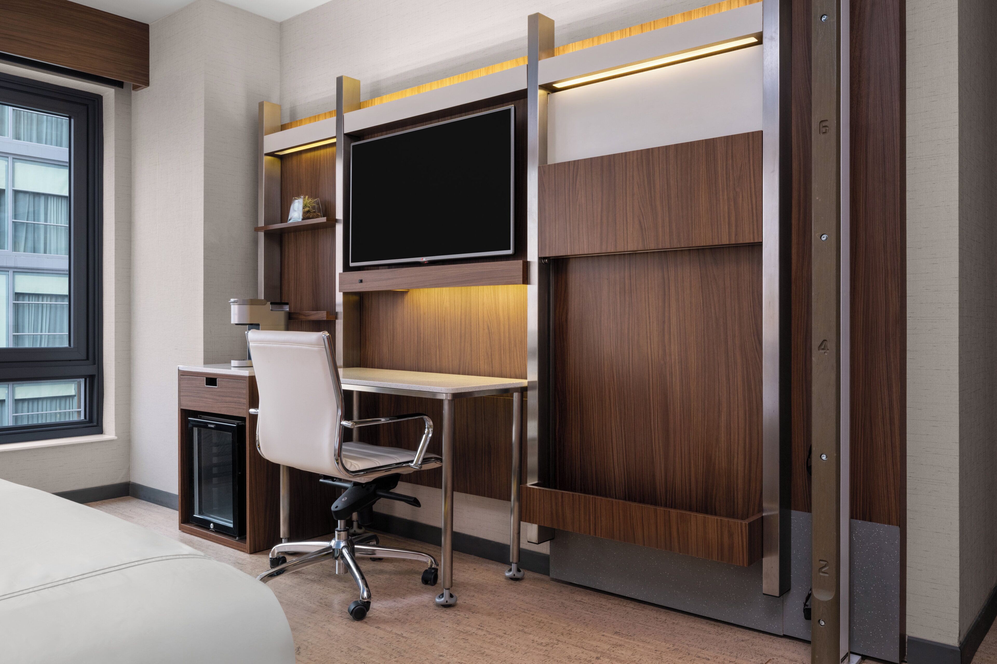Una habitación de hotel moderna con una cama, un escritorio con una computadora, una silla y un ventanal grande.