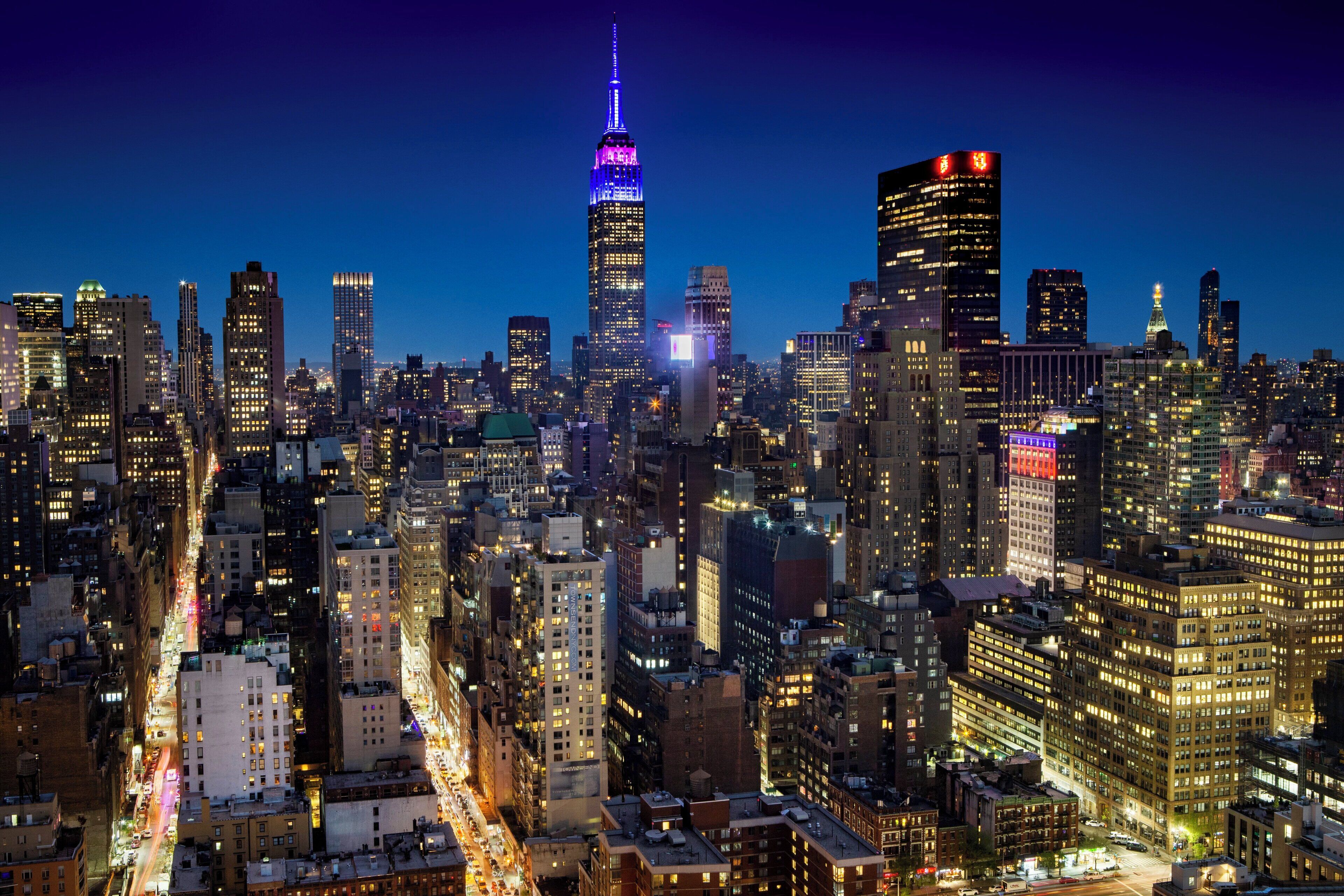 A nighttime cityscape with a prominent skyscraper illuminated in purple and red lights.