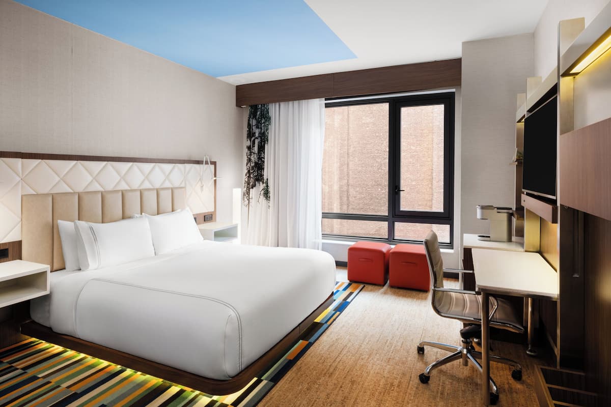 A hotel room with a large bed, a desk, a chair, a TV, and a window with a view of the outside.