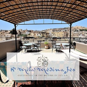 A rooftop terrace with tables and chairs, a pergola, and a view of the cityscape. - R´Mila Medina Fez (Fes)