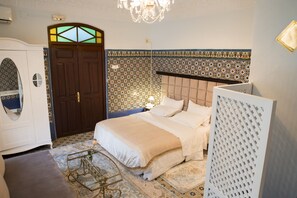 A bedroom with a bed, a wardrobe, a chandelier, and patterned walls.