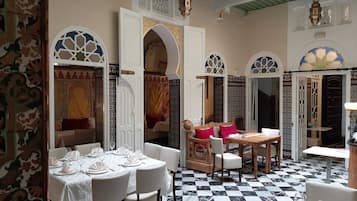 A dining area with tables set for a meal, featuring a checkered floor and ornate arches.