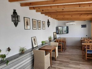 A dining area with wooden tables and chairs, a TV mounted on the wall, and framed pictures on the wall.