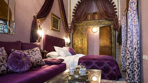 A room with a purple sofa, a glass coffee table with a tray, and a bed with a patterned bedspread.