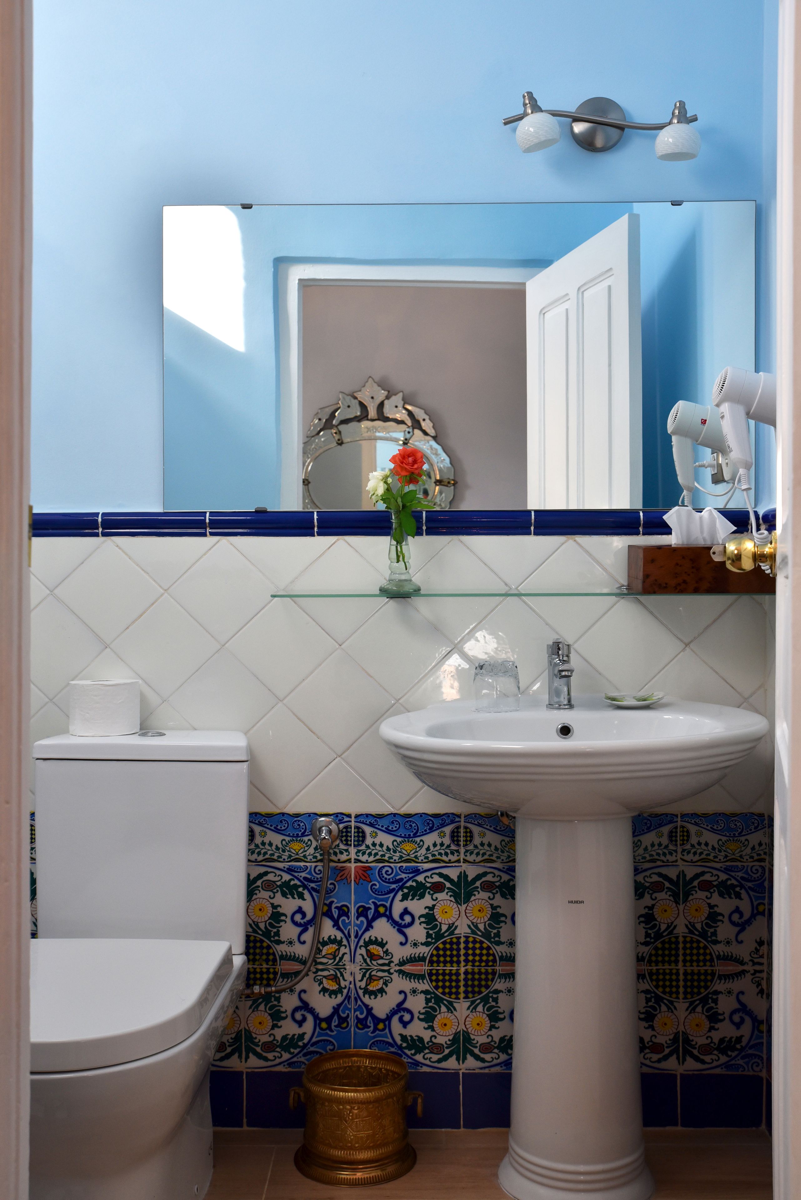 Une salle de bain avec des toilettes blanches, un lavabo sur colonne, un miroir et un espace douche.