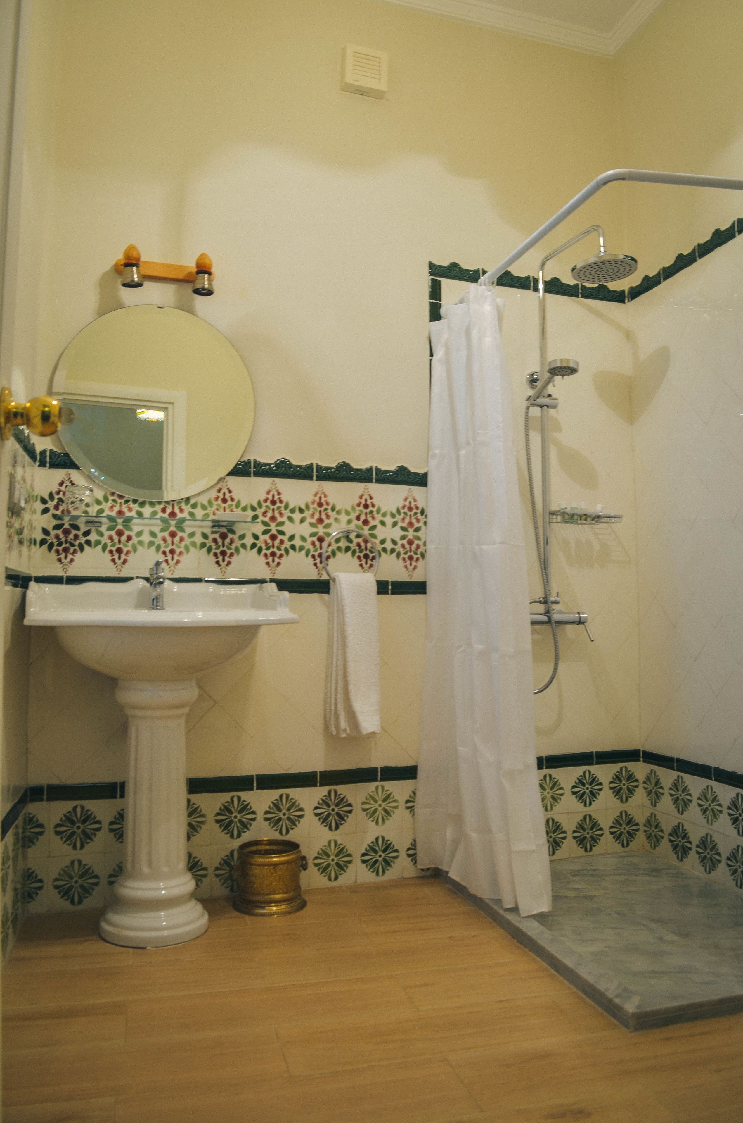 Une salle de bain avec un lavabo blanc, un miroir, une douche équipée d’un pommeau de douche à main et une serviette accrochée au mur.